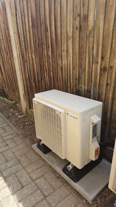 Compact outdoor air conditioning unit installed beside a timber fence